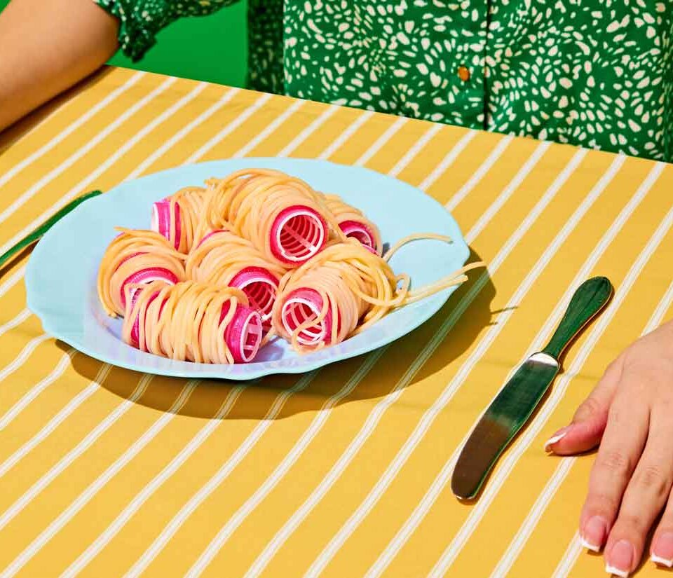 Dame am Esstisch mit Teller gefüllt mit Spaghetti auf Lockenwickler | © shutterstock