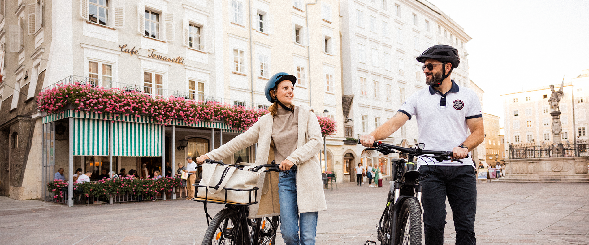 Fotos von einer Frau und einem Mann, die ihre Fahrräder über den Alten Markt in der Altstadt Salzburg schieben.  | © Niko Zuparic