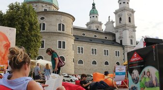 Eine Dame liest in einem Sitzsack am Mozartplatz mit Blick auf den Salzburger Dom ein Buch. | © Innovationswerkstatt - Salzburg im Lesefieber 