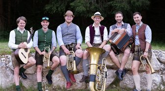 Die Mitglieder der Band G'mahde Wies'n sitzen auf einer Steinmauer. | © Fritz Baumann